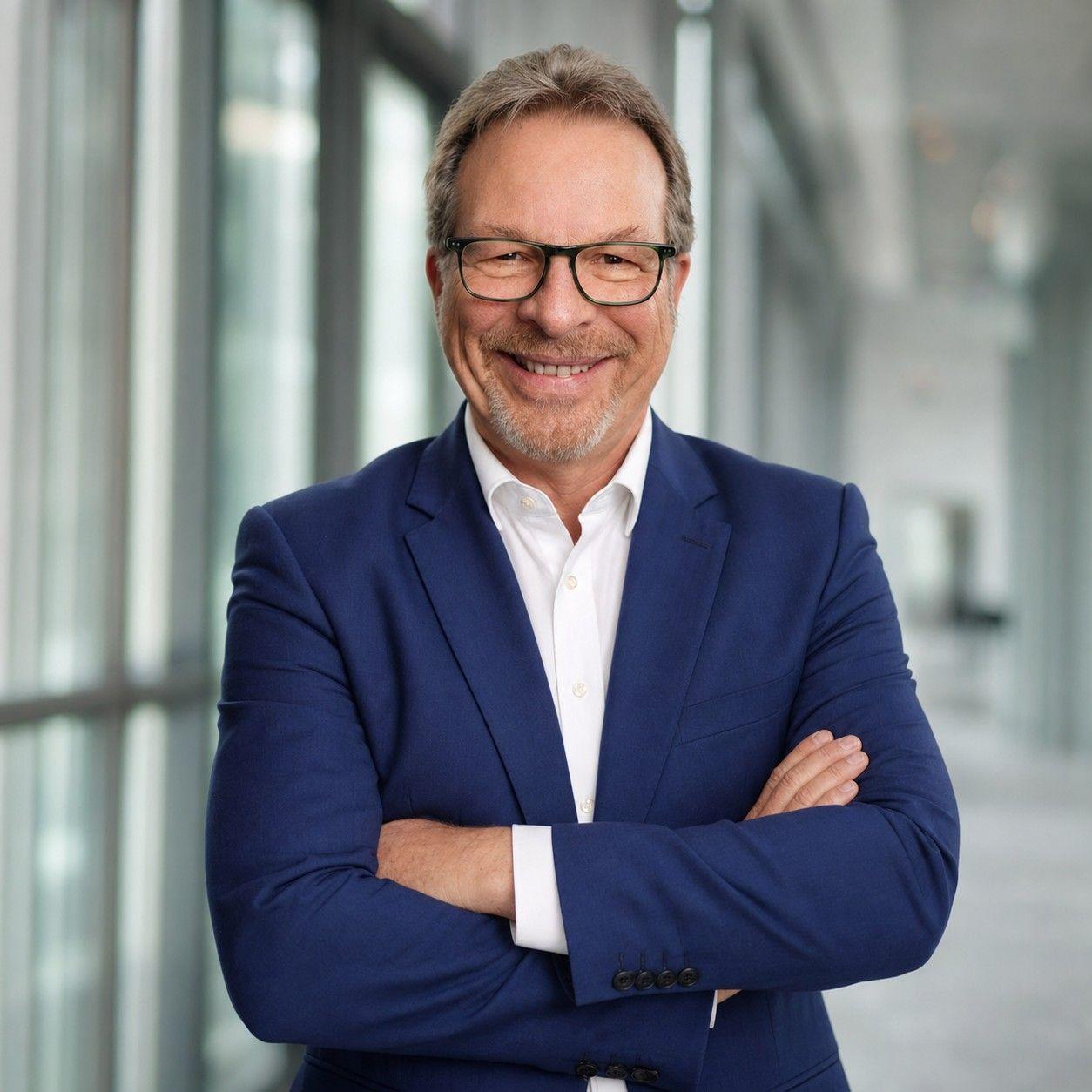 Foto, Bild, Portrait von Alexander Bollmann, Geschäftsführer und Gesellschafter der Management- und Personalberatung BOLLMANN EXECUTIVES. Mann im blauen Anzug mit Brille blickt lächelnd in die Kamera