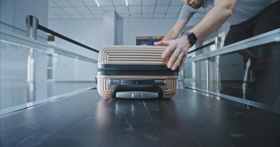 Zu sehen ist die Fördertechnik: Die Hände eines Menschen im kurzärmeligen Hemd heben ein Gepäckstück von einem Kofferband. Ein Kontext zwischen Personalberatung und Fördertechnik.